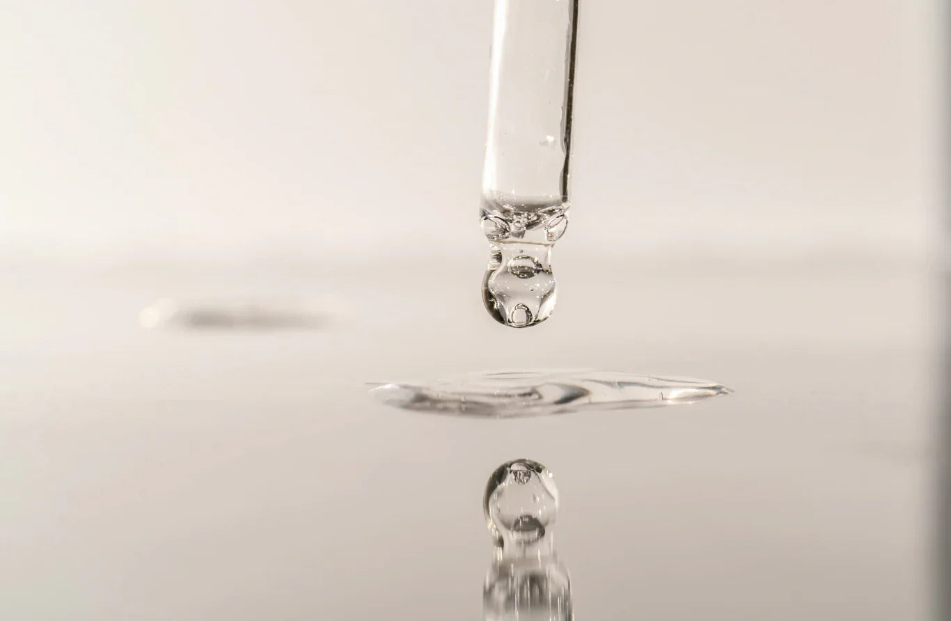 Close-up of serum droplet falling into water on a reflective surface