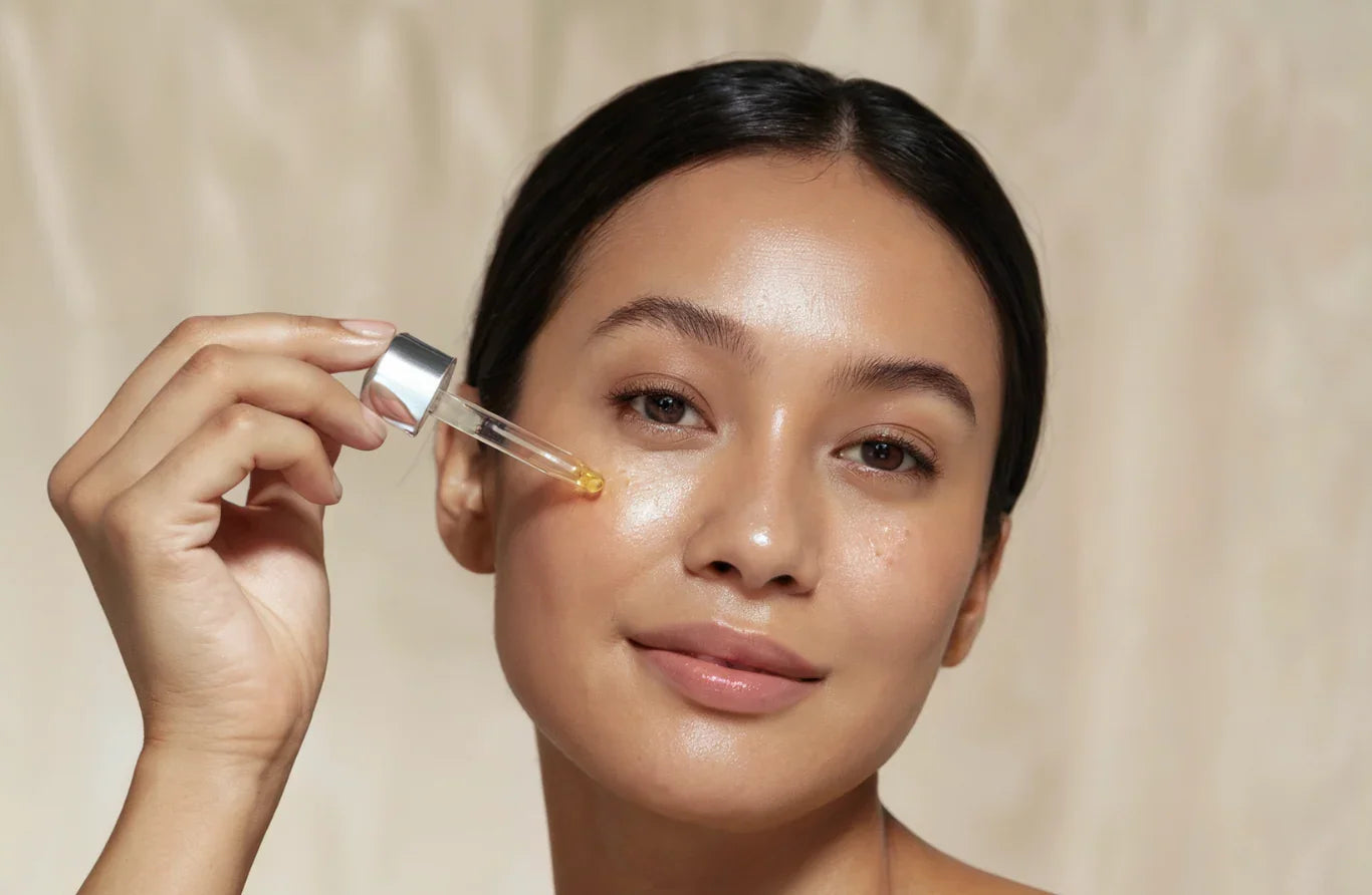 Woman holding a dropper with a clear liquid above her face against a beige background