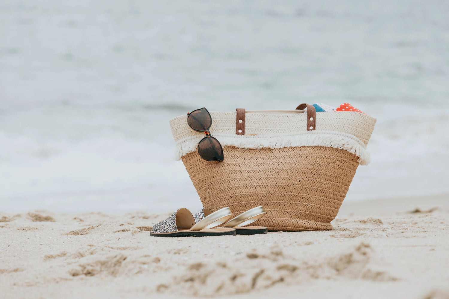 Picture of beach bag and beach contents on sand with water in background.