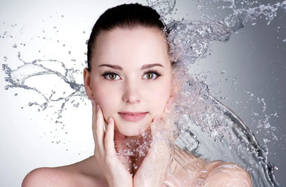 Woman with water splashes around her face on a gray background